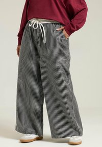 Svart och vitrandiga vida byxor med dragsko i midjan. Tillverkade av lätt viktsmaterial, med avslappnad passform och en mjuk yta.