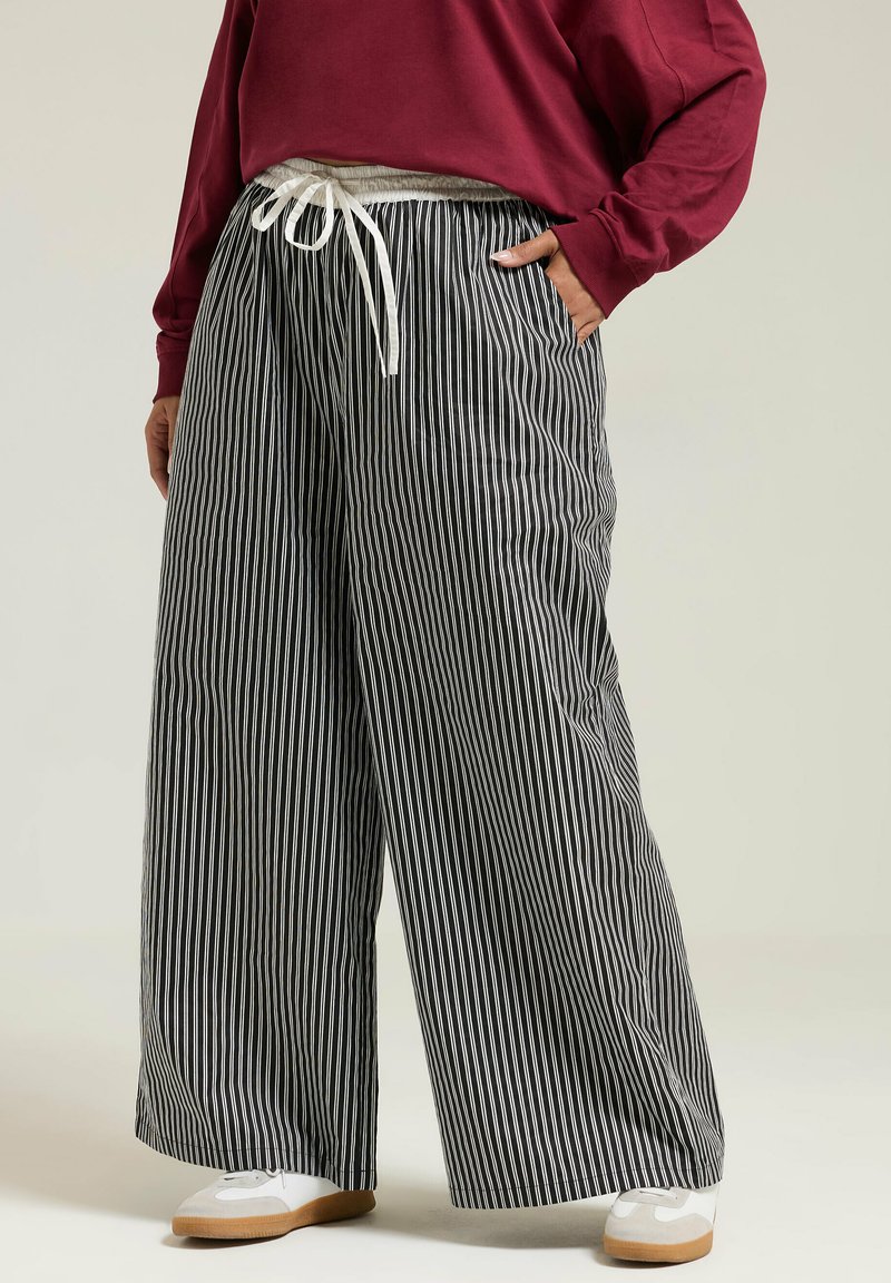 Svart och vitrandiga vida byxor med dragsko i midjan. Tillverkade av lätt viktsmaterial, med avslappnad passform och en mjuk yta.