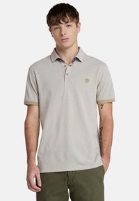 Ljusgrå pikétröja med klassisk krage, som har tre knappar och en kontrasterande blå innerkrage. Inkluderar subtila logotyp- och manschettaccent.