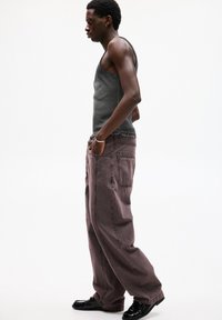 Canottiera grigia, jeans scuri mauve larghi con tasche laterali, orlo sfrangiato e scarpe nere lucide. Design semplice e stile casual.