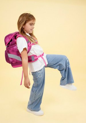 Rosa Rucksack mit grauen Akzenten, getragen von einem Kind. Das Kind trägt ein weißes T-Shirt und eine hellblaue Jeans mit Smileykopf-Grafiken. Der Hintergrund ist gelb.