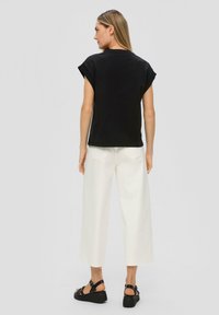 Zwarte T-shirt met korte mouwen en omgeslagen manchetten, gecombineerd met crèmekleurige wijde broek. Zwarte sandalen met rubberen zool maken de outfit compleet.