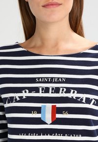 Marinblå och vit randig topp med båthals. Har framsidan med texten "SAINT-JEAN CAP-FERRAT" och ett färgglatt sköldemblem.