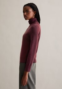 Bordeaux színű, slim fit hosszú ujjú garbó pulóver, puha anyagból készült, szürke csíkos nadrággal párosítva.