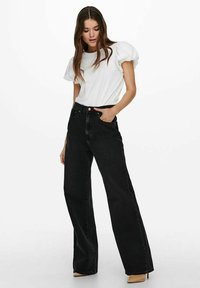 Witte top met pofmouwen gecombineerd met zwart hoge taille wijde broek. De broek heeft een klassiek ontwerp met vijf zakken en een lichte textuur.