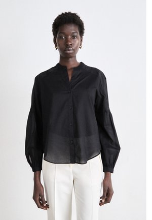 Chemise noire, légère, à boutons et col montant avec des manches longues et volumineuses. Présente une texture légèrement translucide et un ourlet incurvé.