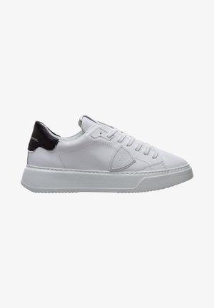 Sneakers en cuir blanc avec un accent noir au niveau du talon, semelle en caoutchouc plate, bout rond, design à lacets et un détail de logo discret sur le côté.