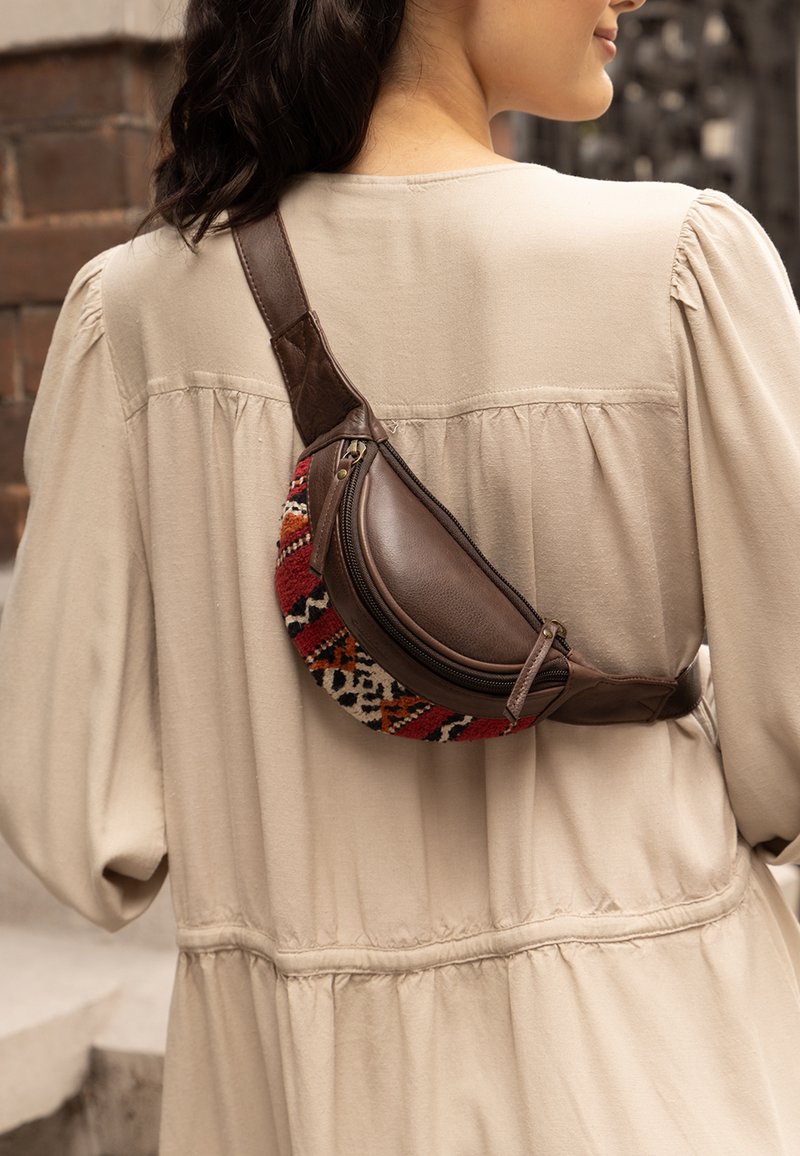 Bruine leren heuptas met een kleurrijke geweven stof met rode, oranje en zwarte patronen, gedragen over een beige top.