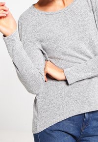 Haut en tricot gris à manches longues avec col rond, coupe décontractée et tissu texturé. Assorti à un jean en denim bleu.