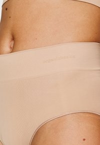Beige seamless high-waisted underwear with a soft texture and minimal stitching. Features an embossed logo on the waistband.