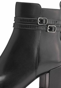 Black leather ankle boot featuring a high block heel, accented with two textured, black faux-crocodile straps and silver buckles.