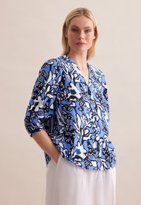 Luftige Bluse in Blau und Schwarz mit Muster, V-Ausschnitt und umgeschlagenen Ärmeln, die abstrakte Blumenmuster und leichten Stoff aufweist.