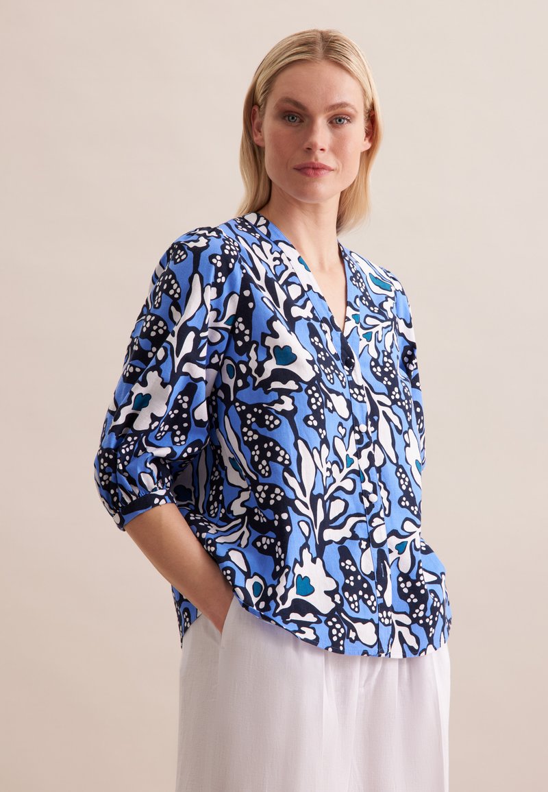 Luftige Bluse in Blau und Schwarz mit Muster, V-Ausschnitt und umgeschlagenen Ärmeln, die abstrakte Blumenmuster und leichten Stoff aufweist.