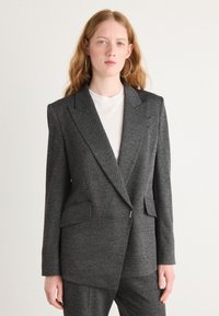 Blazer ajusté gris en motif chevron, avec de grands revers, deux poches latérales et une fermeture à un bouton. Texture lisse.