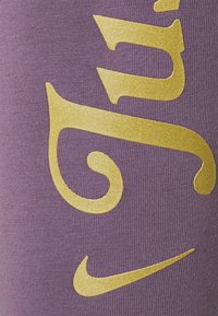 Lila textil med en slät yta pryds av djärva, glittrande guld-texter och en liten gyllene Nike-logotyp i det nedre hörnet.