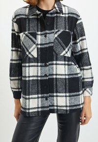 Shacket a quadri bianco e nero con chiusura a bottoni, due tasche sul petto e maniche lunghe. Realizzato in un morbido tessuto testurizzato.