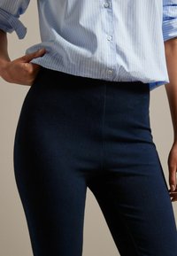 Marineblauwe high-waisted leggings met een gladde textuur, met een aansluitend ontwerp. Gekenmerkt door een lichtblauwe, verticaal gestreepte blouse met knopen.