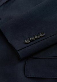 Ärmel eines Marineblazers mit strukturierter Innenfutter, vier schwarzen Knöpfen am Ärmelabschluss und einem klassischen Kerbkragen.