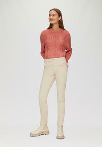 Pull en tricot corail avec un motif texturé, associé à un pantalon crème ajusté et des bottines beige à semelle épaisse.