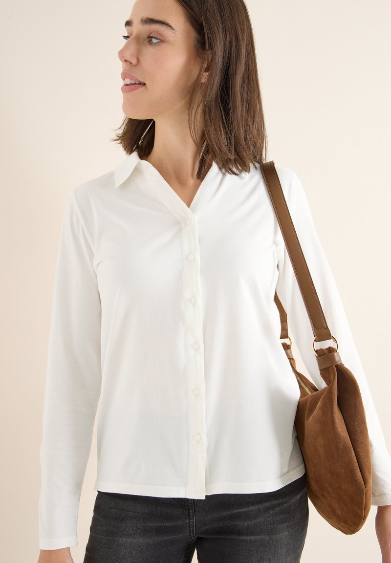 Weißes Langarm-Hemd mit Knopfleiste und Kragen, kombiniert mit einer Schultertasche aus braunem Wildleder. Einfaches Design mit glatter Textur.