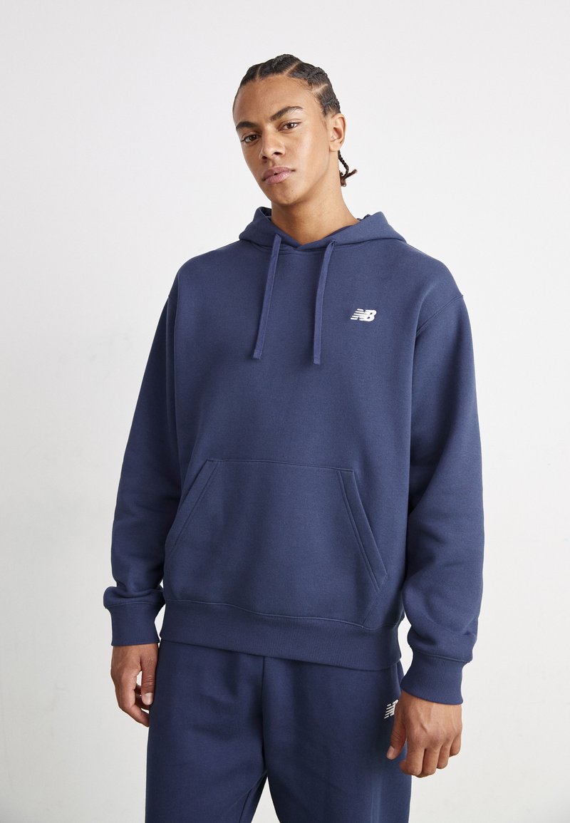 Marineblå hettegenser laget av myk stoff med en frontlomme og en liten hvit logo på brystet. Regular fit med ribbestrikkede mansjetter.