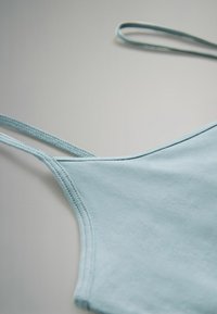 Hellblaues Tanktop mit dünnen Trägern, aus weichem Stoff gefertigt, mit glatter Textur und sauberen Nähten. Minimalistisches Design, ohne Muster.