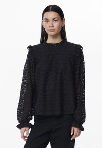 Svart bluse med teksturert mønster, volangkrage og mansjetter, lange ermer og en avslappet passform, laget av et lett, gjennomsiktig materiale.