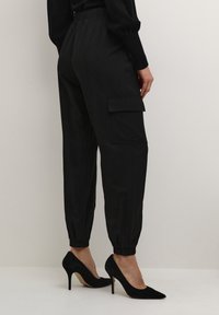 Black cargo pants with an elastic waistband, cuffed hems, side pockets, paired with pointed black suede heels. Smooth texture.