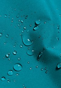 Tessuto impermeabile color teal con gocce d'acqua visibili che si formano in perle sulla superficie, mostrando una trama liscia e una tessitura stretta.