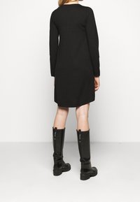 Abito nero a maniche lunghe realizzato in un materiale morbido, caratterizzato da un collo rotondo e un orlo leggermente svasato, abbinato a stivali di gomma neri al ginocchio.