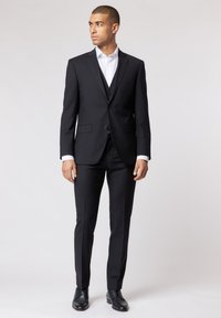Czarny garnitur o dopasowanym kroju, z dwoma guzikami w marynarce, klapami typu notch oraz spodniami typu flat-front, w połączeniu z biał�ą koszulą i czarnymi butami.