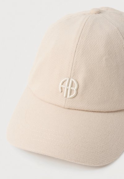Beige baseballpet met gebogen klep en geborduurd wit "AB"-logo op het voorpaneel, gemaakt van gestructureerde stof.