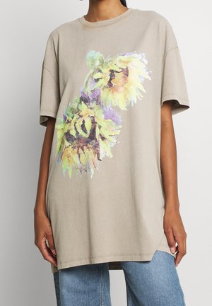 Beige oversized T-shirt med stort, farverigt motiv af en solsikke, båret med lyseblå jeans.