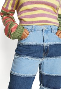 Vaqueros de mezclilla azul con rayas horizontales de mezclilla clara y oscura, con bordes deshilachados y un diseño de talle alto.