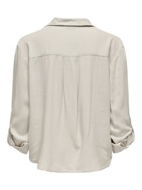 Camisa beige de manga larga con mangas remangadas, detalle en el canesú trasero y un pliegue central que proporciona un ajuste holgado y relajado.