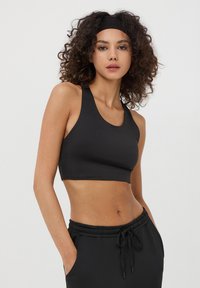 Top sportivo nero a crop con scollatura rotonda e spalline larghe, realizzato in materiale liscio e elasticizzato, abbinato a pantaloni sportivi neri coordinati.