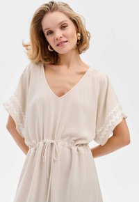 Beige, lichtgewicht jurk met een V-halslijn, korte geflonterde mouwen met witte golvende afwerking en een trekkoordin de taille.