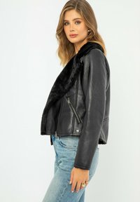 Giacca di pelle nera con colletto in pelliccia sintetica; chiusura con zip asimmetrica; leggera, texture liscia; design aderente; elementi di stile classici.