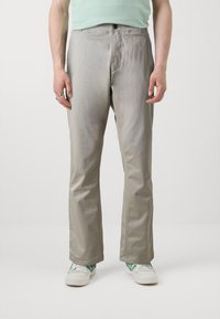 Gaišpelēku, taisnu kāju bikses, kas izgatavotas no gludas auduma; iekļauj priekšu kabatas un rāvējslēdzēja aizdari, apvienotas ar baltām kedām ar zaļiem akcentiem.