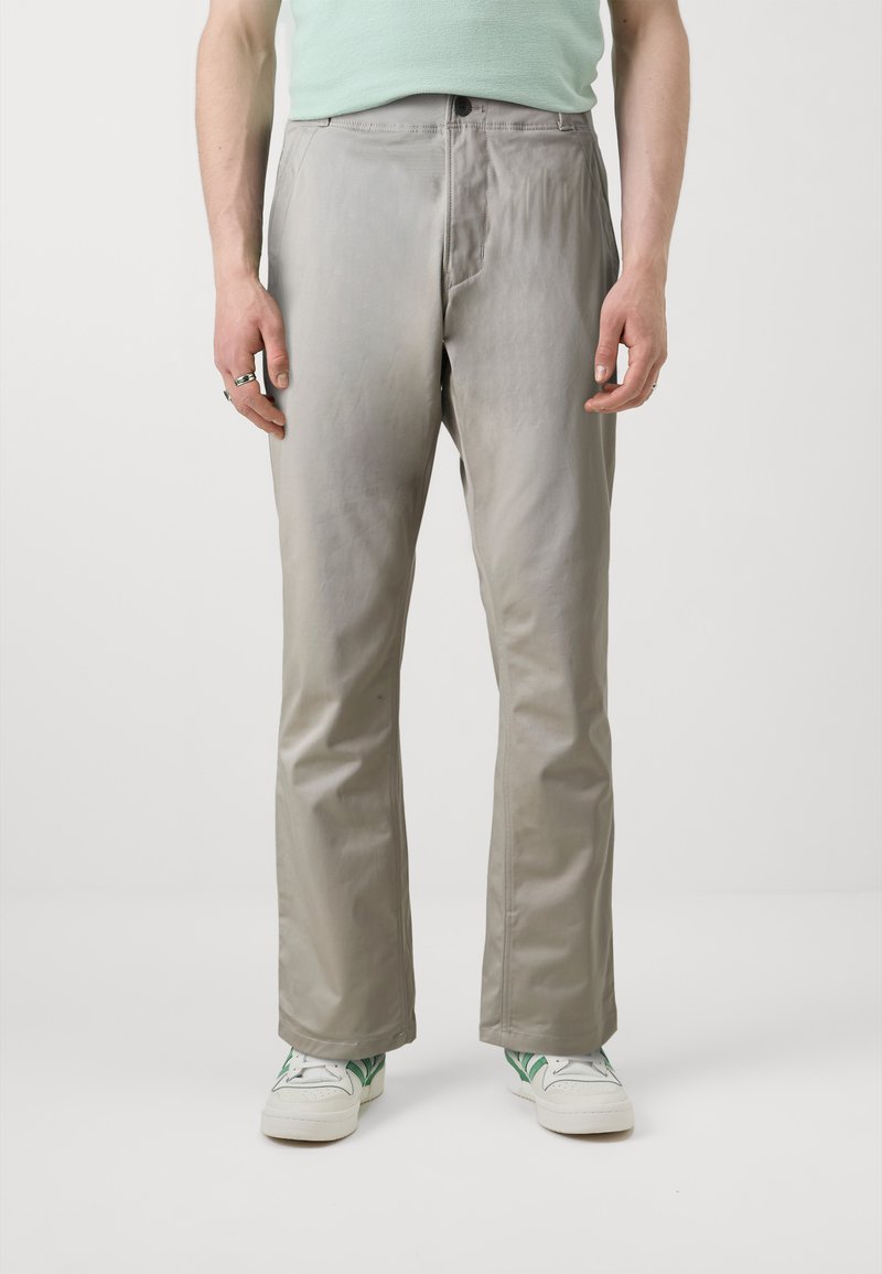 Gaišpelēku, taisnu kāju bikses, kas izgatavotas no gludas auduma; iekļauj priekšu kabatas un rāvējslēdzēja aizdari, apvienotas ar baltām kedām ar zaļiem akcentiem.