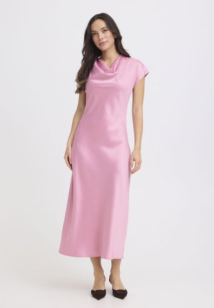 Donna con capelli lunghi e scuri che indossa un vestito midi rosa in raso senza maniche e tacchi neri con punta a punta, in piedi su uno sfondo bianco.