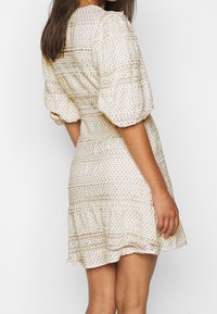 Vestido color crema con mangas abullonadas, tejido texturizado y rayas horizontales. Presenta pequeños lunares y un dobladillo en capas.