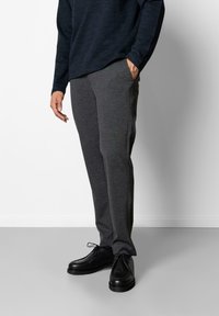 Dunkelgraue Jogginghose mit schmalem Schnitt, aus weichem Stoff. Kombiniert mit schwarzen Lederschuhen, die ein texturiertes Obermaterial und Schnürsenkel aufweisen.