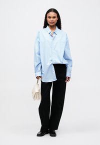 Camisa oversized azul e branca com riscas, combinada com calças largas pretas e uma bolsa creme. Tecido suave, ajuste descontraído.