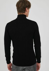 Fekete pulóver, magas gallérral, texturált cikk-cakk mintával, bordázott mandzsettákkal és testhezálló fazonnal.