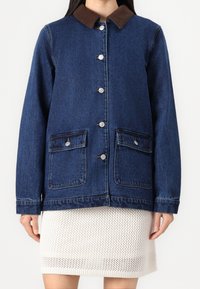 Mörkblå denimjacka med en brun kordflodds-kra. Den har silverfärgade tryckknappar, två framfickor och en avslappnad passform.