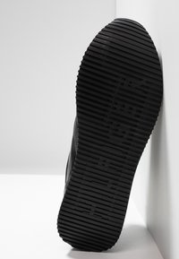 Černá gumová podrážka boty s horizontálními drážkami a rýhami, ukazující strukturovaný vzor pro lepší grip; okraj je hladký a zaoblený.