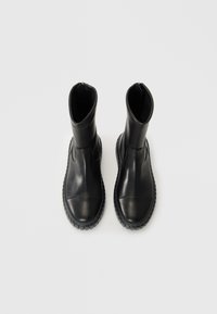 Bottes en cuir noir avec une texture lisse, dotées d'un bout arrondi et d'une semelle en caoutchouc, hauteur au-dessus de la cheville et fermeture à glissière sur le côté.