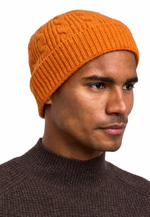 Oranje gebreide beanie met een geribbelde textuur en kabelontwerp. Draagt op het hoofd met een close-up van het gezicht en een donkerbruine trui.