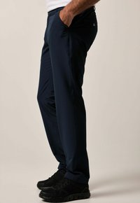 Marinblå byxor med sidofickor, slim fit och en slät tygkvalitet. Kombineras med svarta träningsskor.